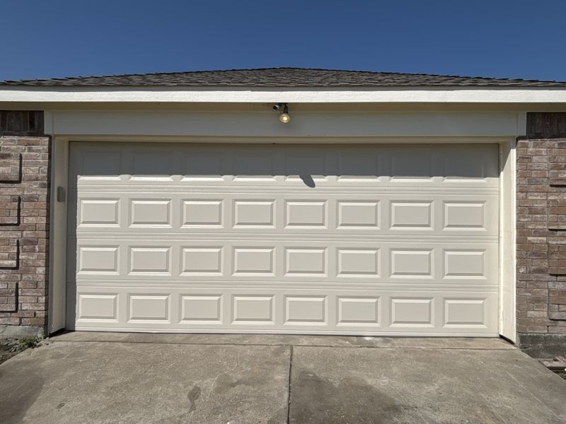 Almond raised-panel double garage door after a repair in Farmersville, TX