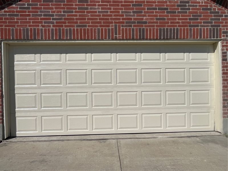 New almond raised-panel double garage door on a brick home in Fate, TX